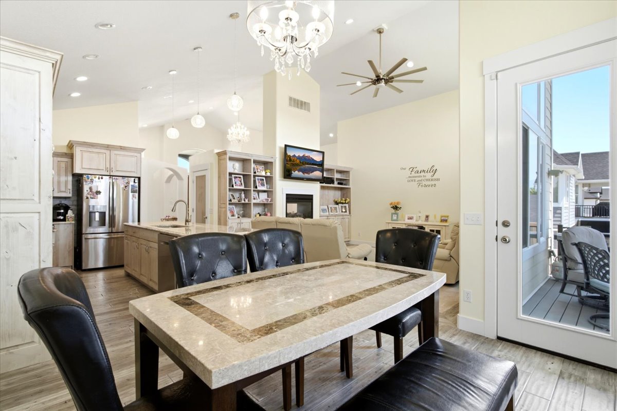 Open concept living space featuring a central dining area with a stone-top table, a kitchen island with sink and stainless steel appliances, and a living area with a fireplace