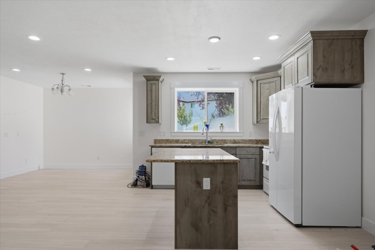 Open-concept kitchen featuring wood-finish cabinetry, granite countertops, an island with seating potential, and recessed lighting