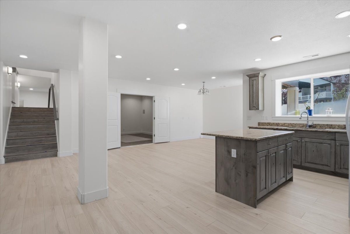 Open-concept living area featuring light wood-finish flooring, recessed lighting, and a kitchen island with a stone-finish countertop