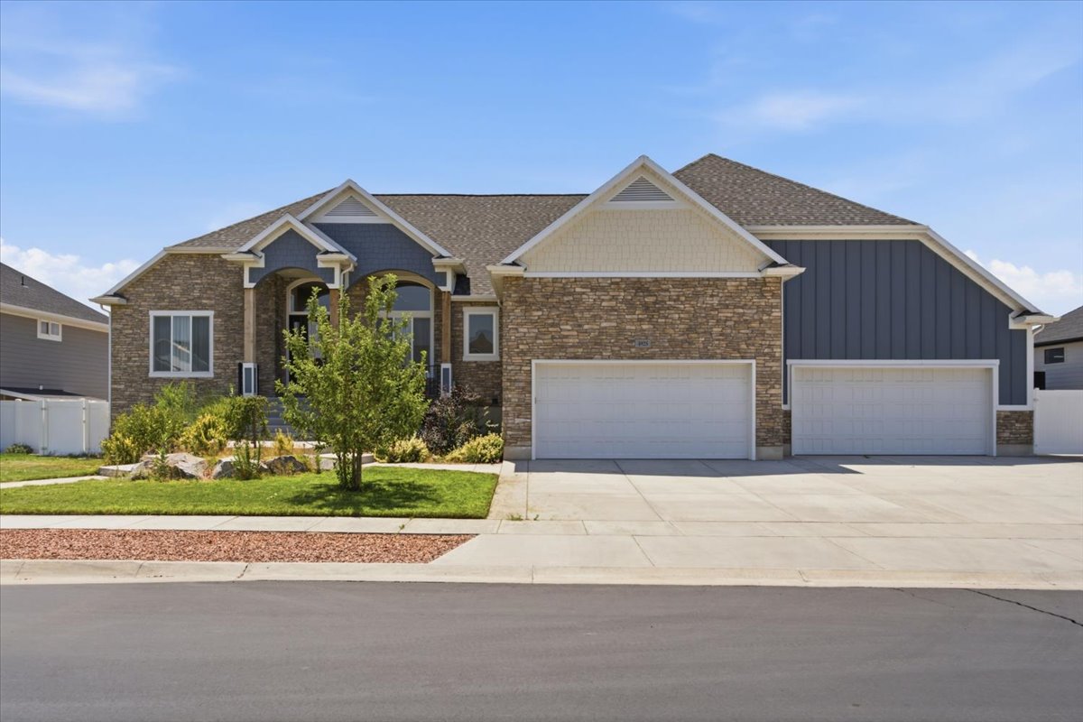 Stone and siding exterior with a multi-car garage, manicured lawn, and mature landscaping