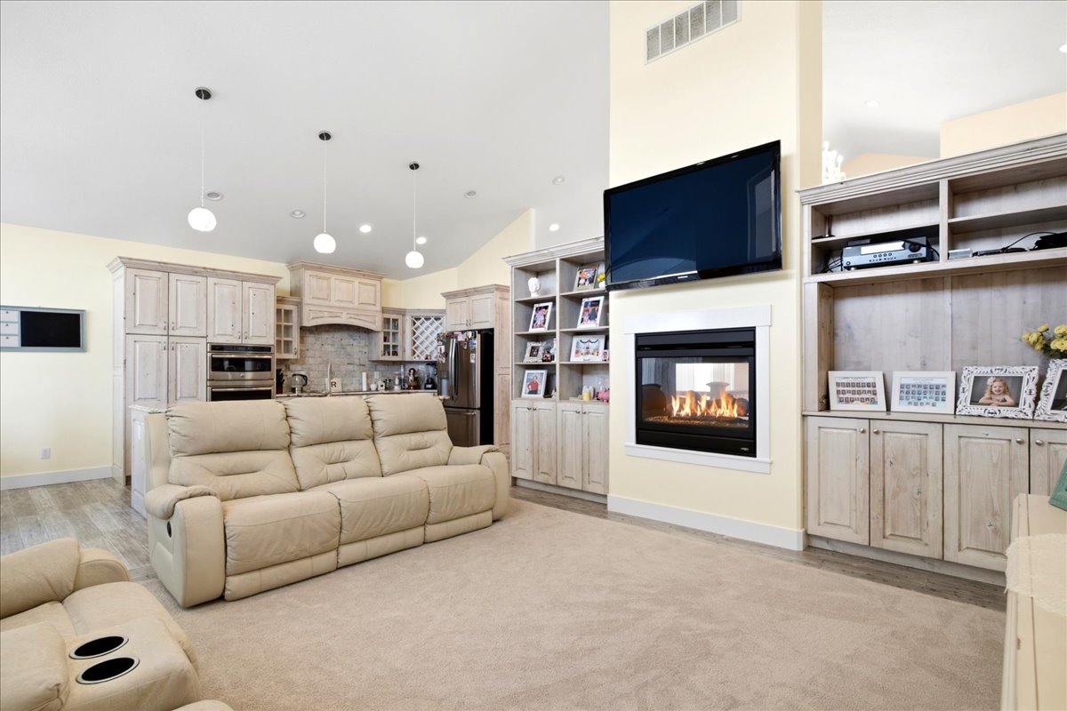 Integrated living space featuring a built-in fireplace, custom built-in cabinetry, and a kitchen area with light-toned wood-finish cabinetry