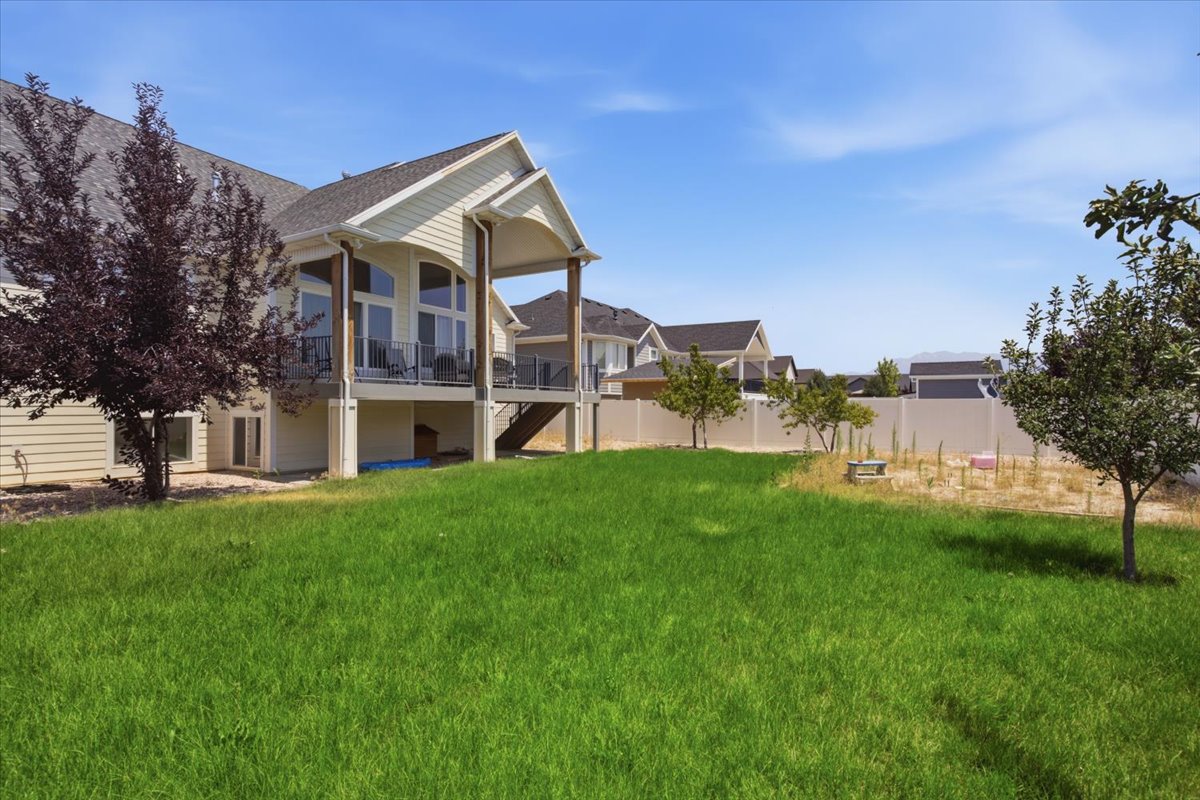 Rear exterior featuring a covered deck with glass panel railings, large arched windows, and a walk-out patio