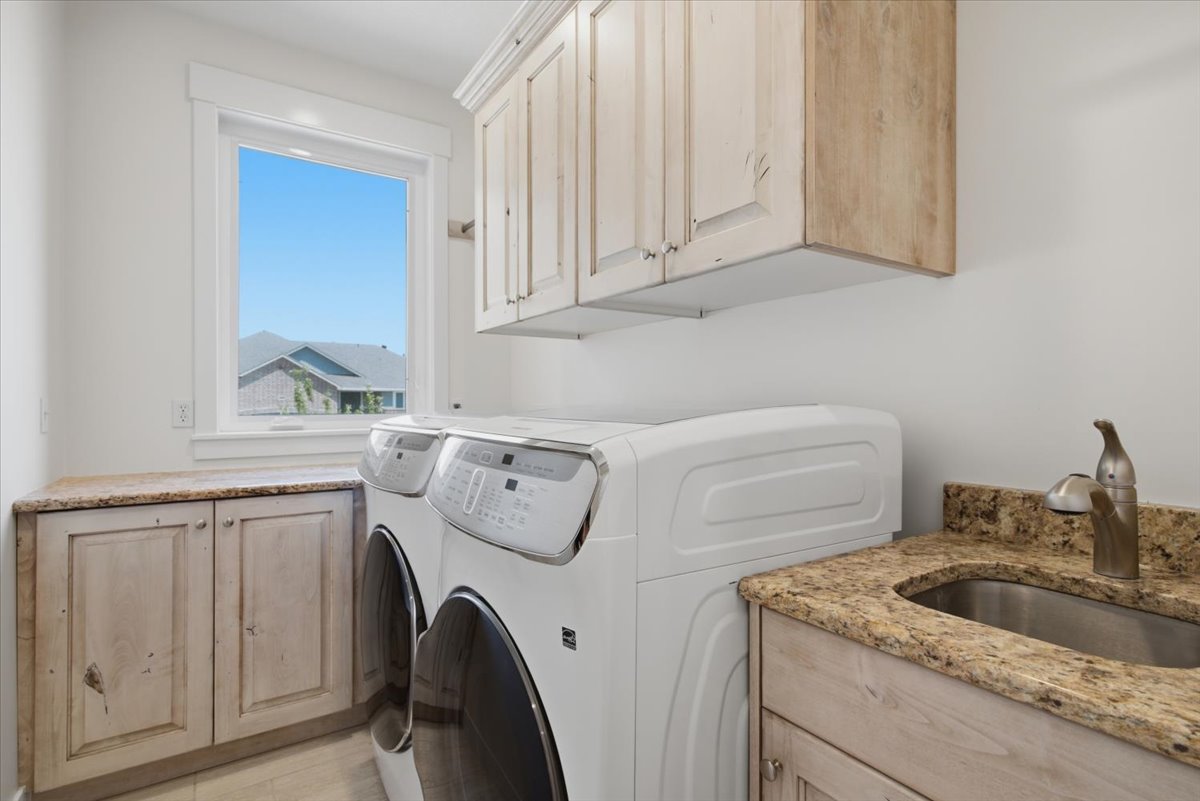 Laundry area featuring light-toned cabinetry, a built-in sink with a countertop, upper storage cabinets, and a window providing natural light