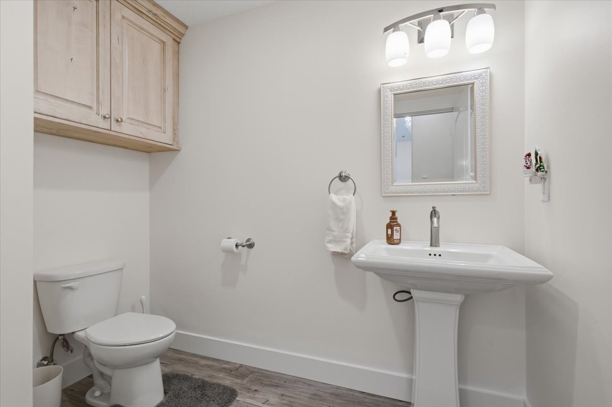 Bathroom featuring a pedestal sink, wall-mounted mirror with decorative frame, overhead three-light vanity fixture, and light-toned wood-finish flooring