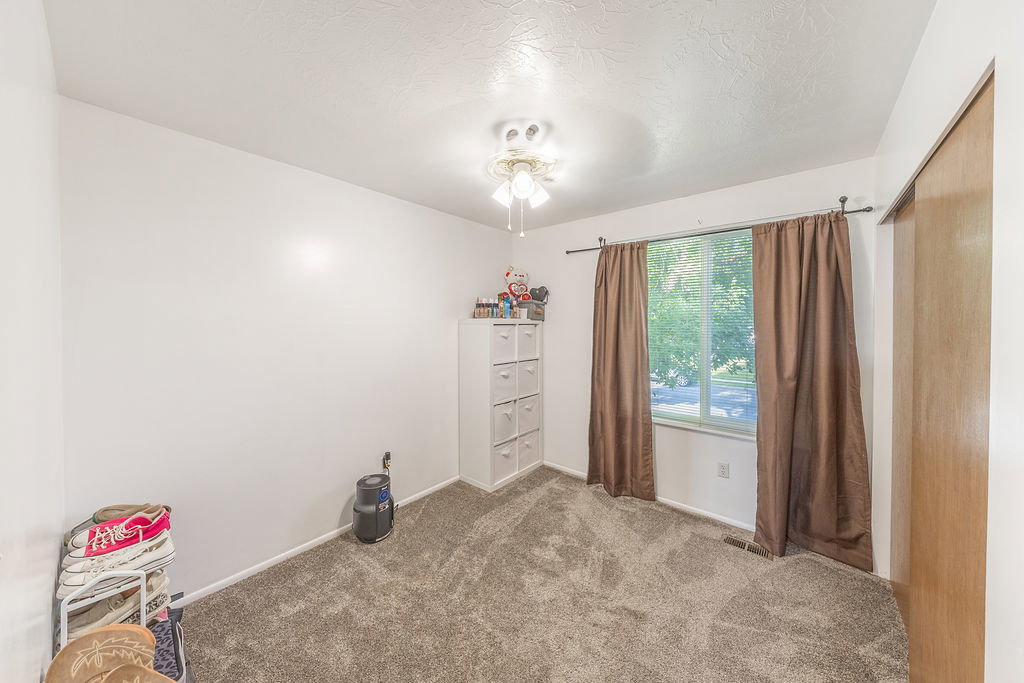 Carpeted room featuring a window with exterior views, a ceiling fan with integrated lighting, and a sliding wood-finish closet door