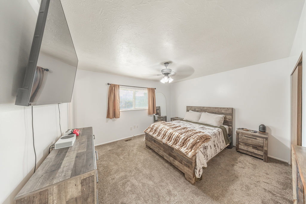 Carpeted bedroom featuring a ceiling fan with light fixture, window with curtains, and a built-in closet with wood-finish door