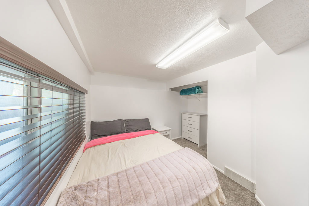 Bedroom featuring a window with horizontal blinds, overhead fluorescent lighting, and wall-to-wall carpeting