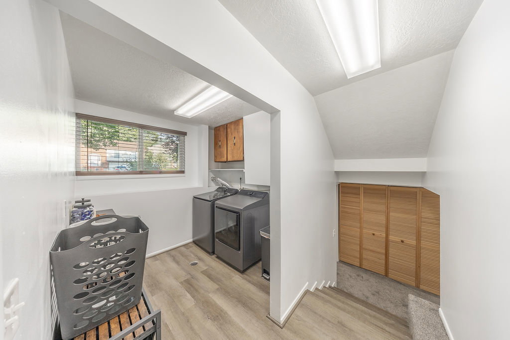 Dedicated laundry area featuring a window, overhead cabinetry, and wood-finish flooring