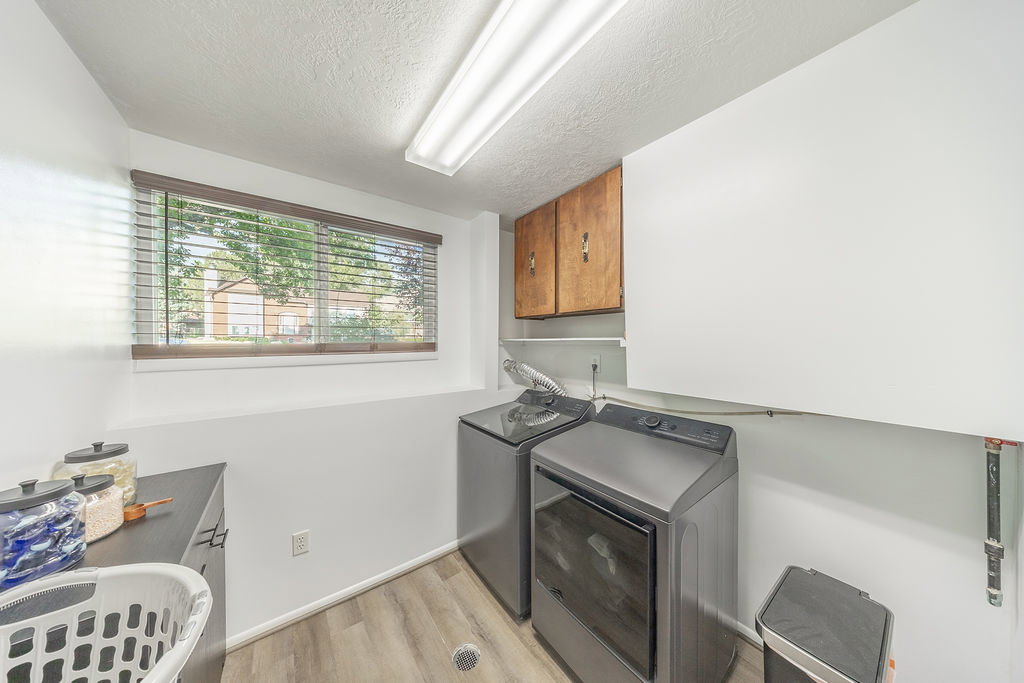 Laundry area featuring wood-finish flooring, a rectangular window with blinds, and built-in upper cabinetry