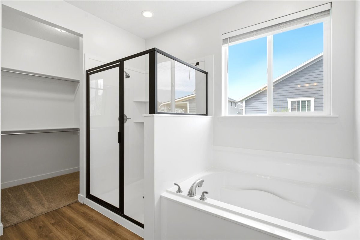 Contemporary bathroom featuring a black-framed glass shower enclosure, built-in soaking tub with chrome fixtures, and a dual-pane window