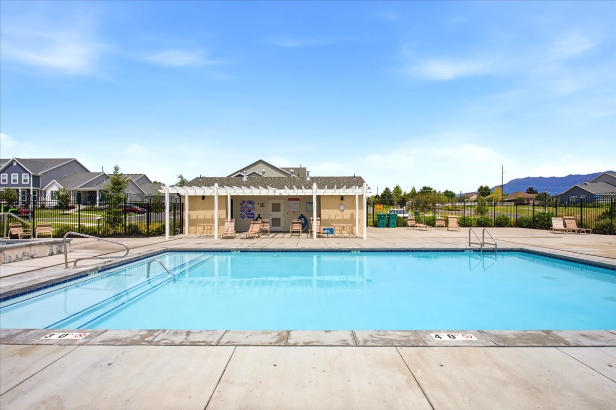 Community swimming pool with concrete decking, perimeter fencing, and a shaded pergola structure