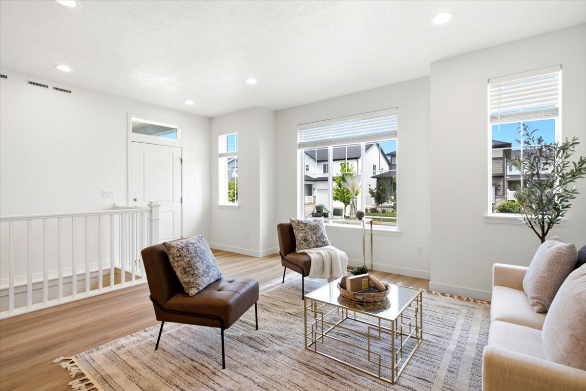 Living area featuring large windows, wood-finish flooring, a white spindle railing, recessed lighting, and a white entry door with a transom window