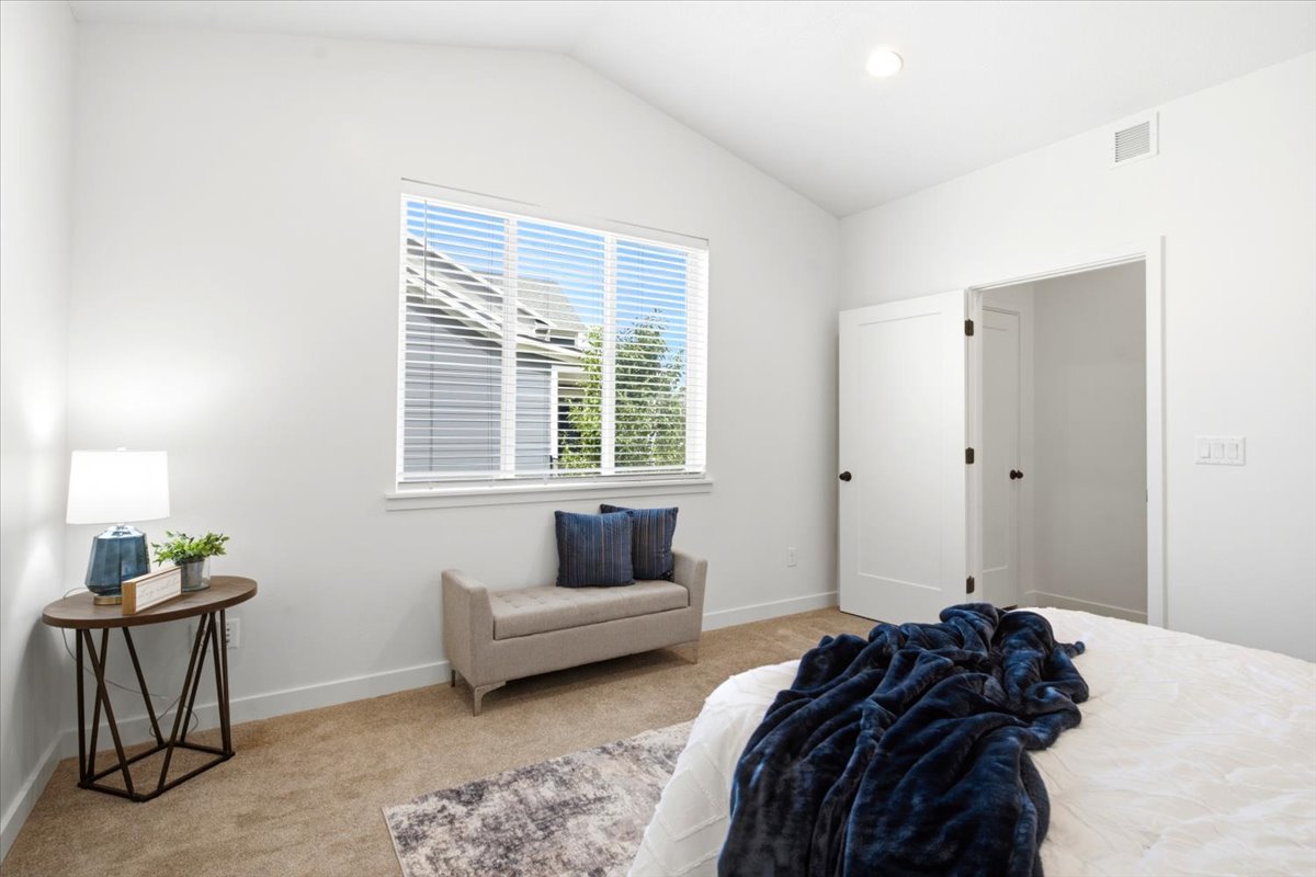 Spacious room featuring vaulted ceilings, a large window, neutral carpet flooring, and white interior doors with black hardware