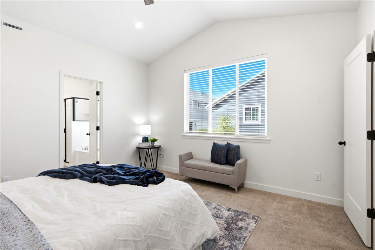 Vaulted ceiling bedroom with a large window featuring horizontal blinds
