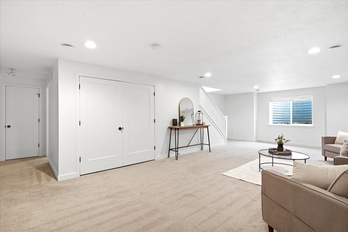 Spacious lower-level living area featuring neutral carpeting, recessed lighting, and a white staircase with matching railing