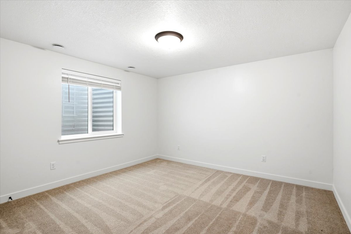 Carpeted room featuring a single window with blinds, white walls, and a ceiling-mounted light fixture