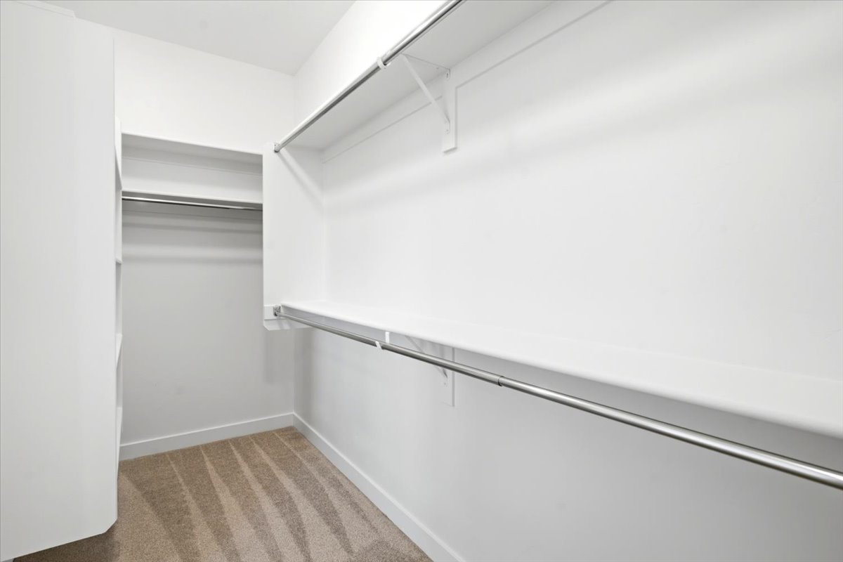 Walk-in closet featuring white walls, white shelving, and chrome hanging rods