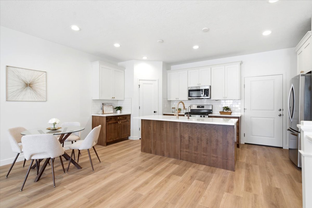 Open-concept kitchen and dining area featuring light wood-finish flooring, white cabinetry, a wood-finish island with a light-toned countertop, stainless steel appliances, and recessed lighting