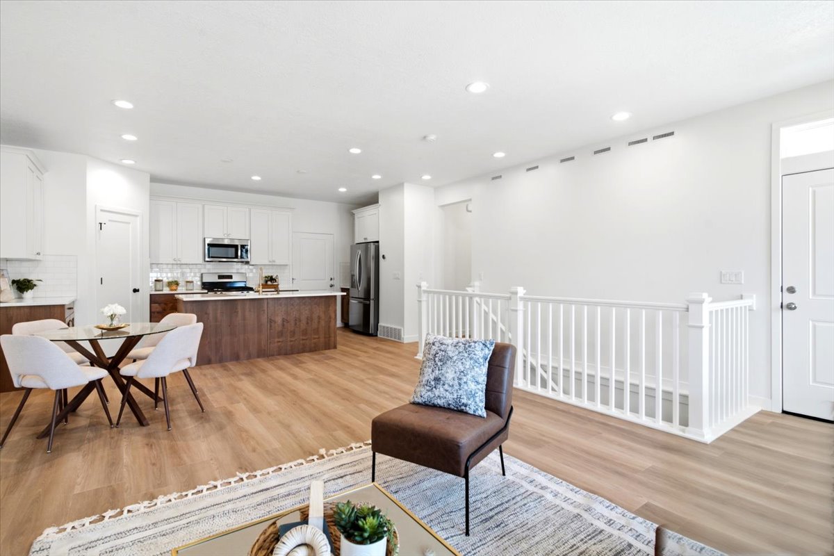 Open-concept living area featuring wood-finish flooring, recessed lighting, a kitchen with white cabinetry and stainless steel appliances, a wood-finish kitchen island, and a white staircase with balusters