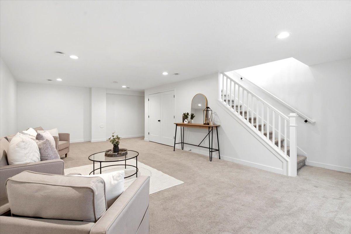 Spacious carpeted room featuring recessed lighting, white walls, and a staircase with white balusters and handrails