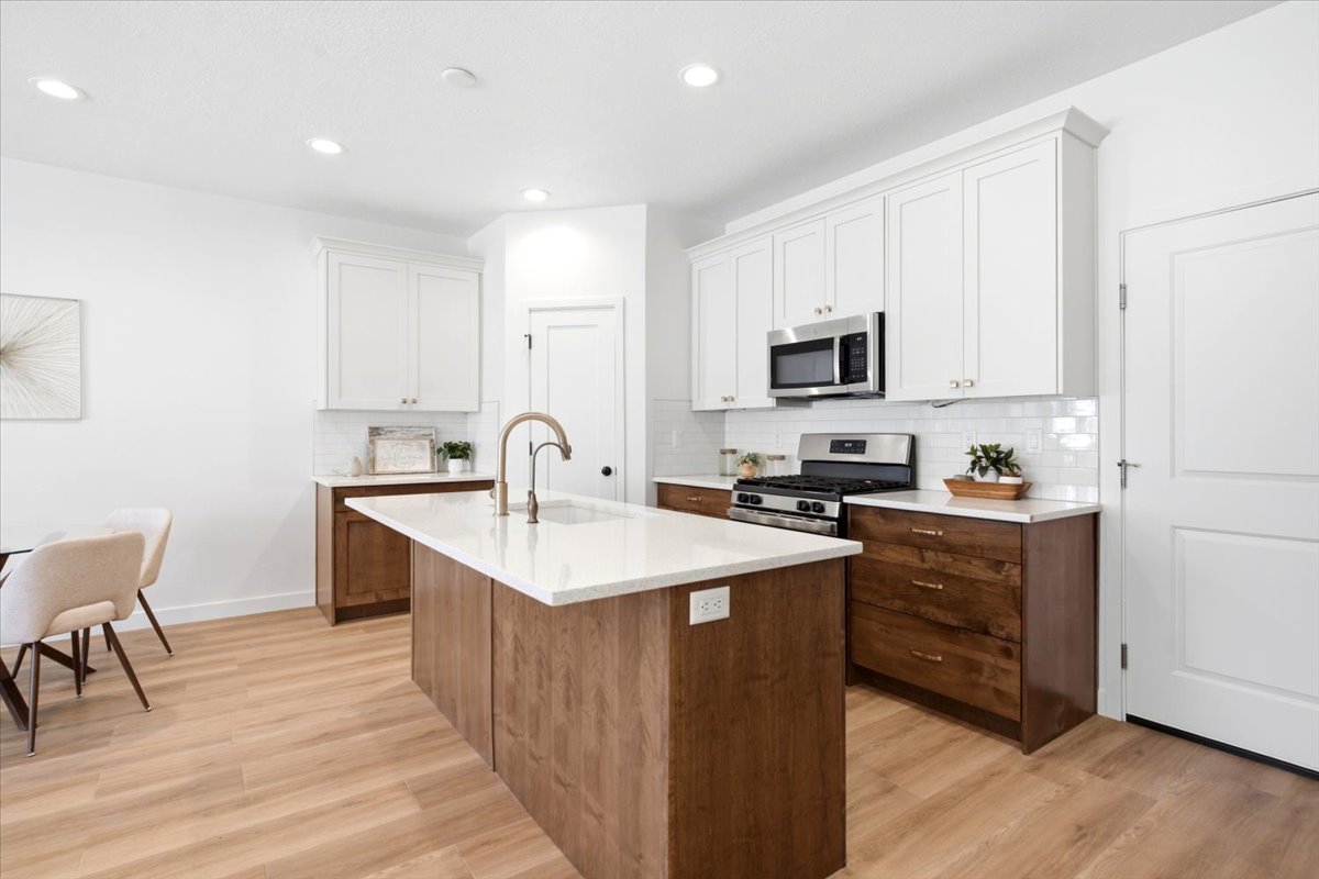 Kitchen featuring a central island with a light-toned countertop and integrated sink, stainless steel appliances, white subway tile backsplash, two-tone cabinetry, and wood-finish flooring