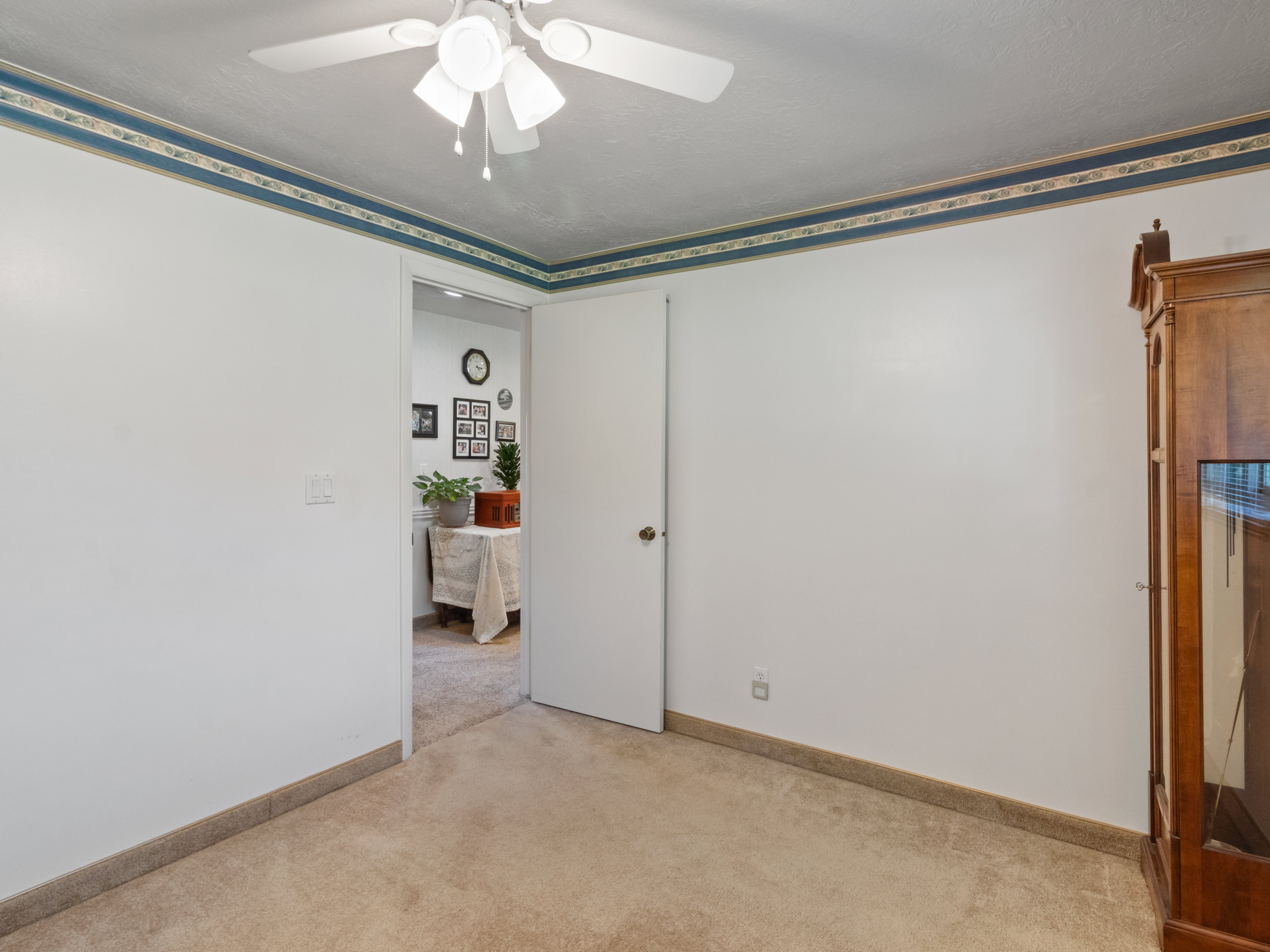 Carpeted room featuring white walls with a decorative border, a ceiling fan, and a light-colored door