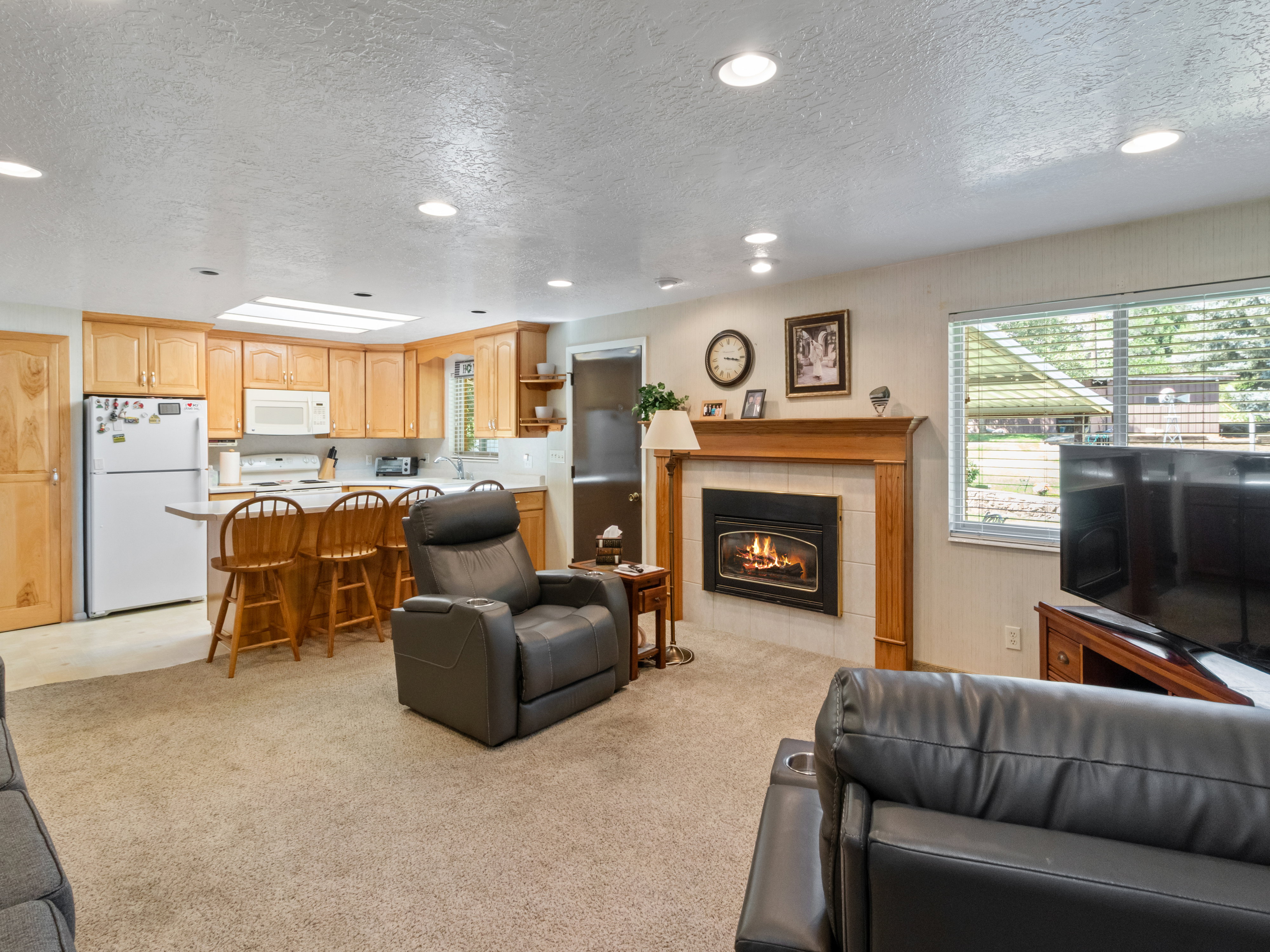 Living area featuring a gas fireplace with a wood mantle and tile surround, recessed lighting, and a kitchen with wood cabinetry and a breakfast bar