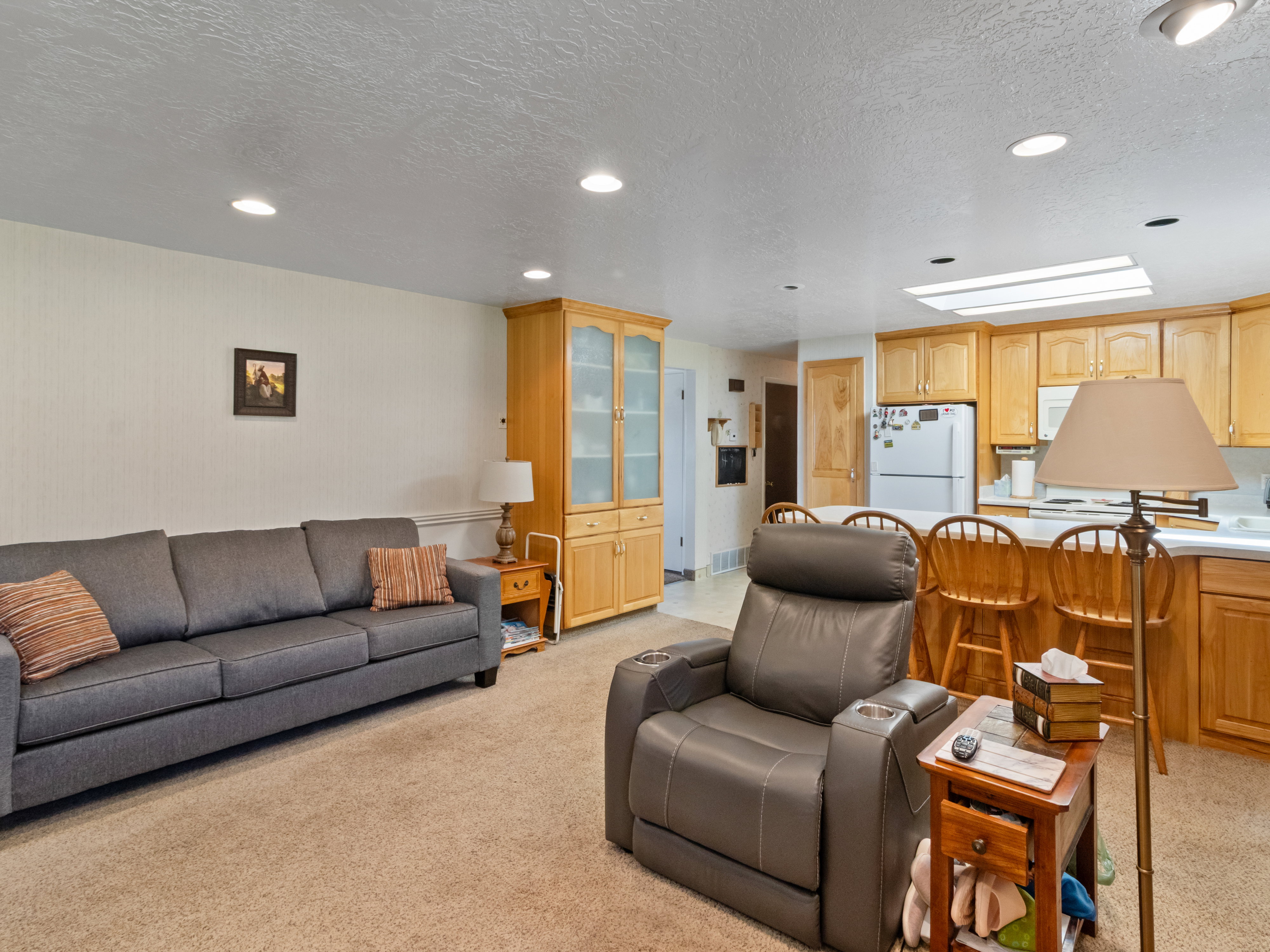 Open-concept living space featuring recessed lighting, plush carpet flooring, a built-in display cabinet with glass doors, a kitchen island with seating, and a full suite of kitchen appliances