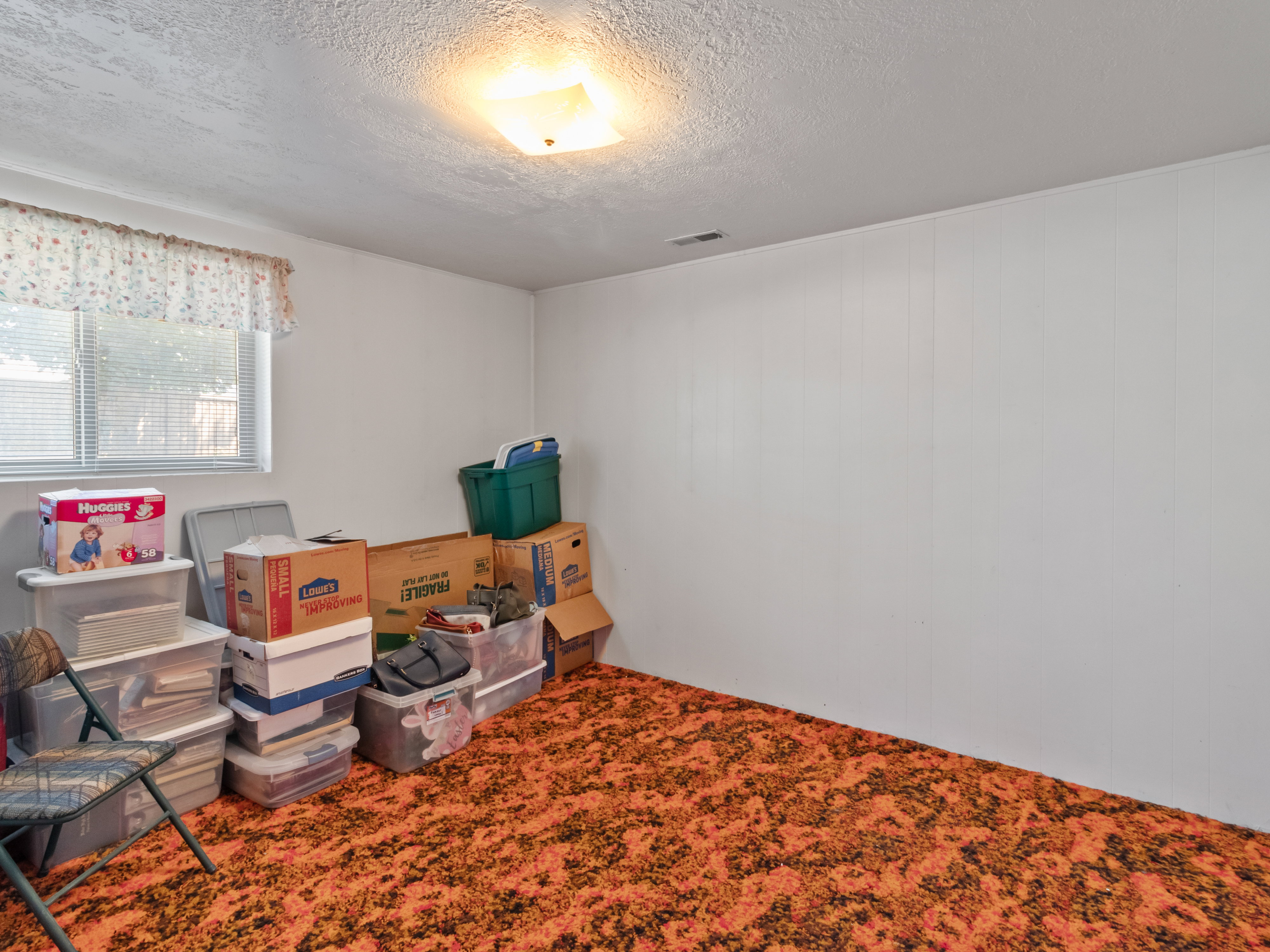 Room featuring orange and black patterned carpet, white paneled walls, and a window with blinds