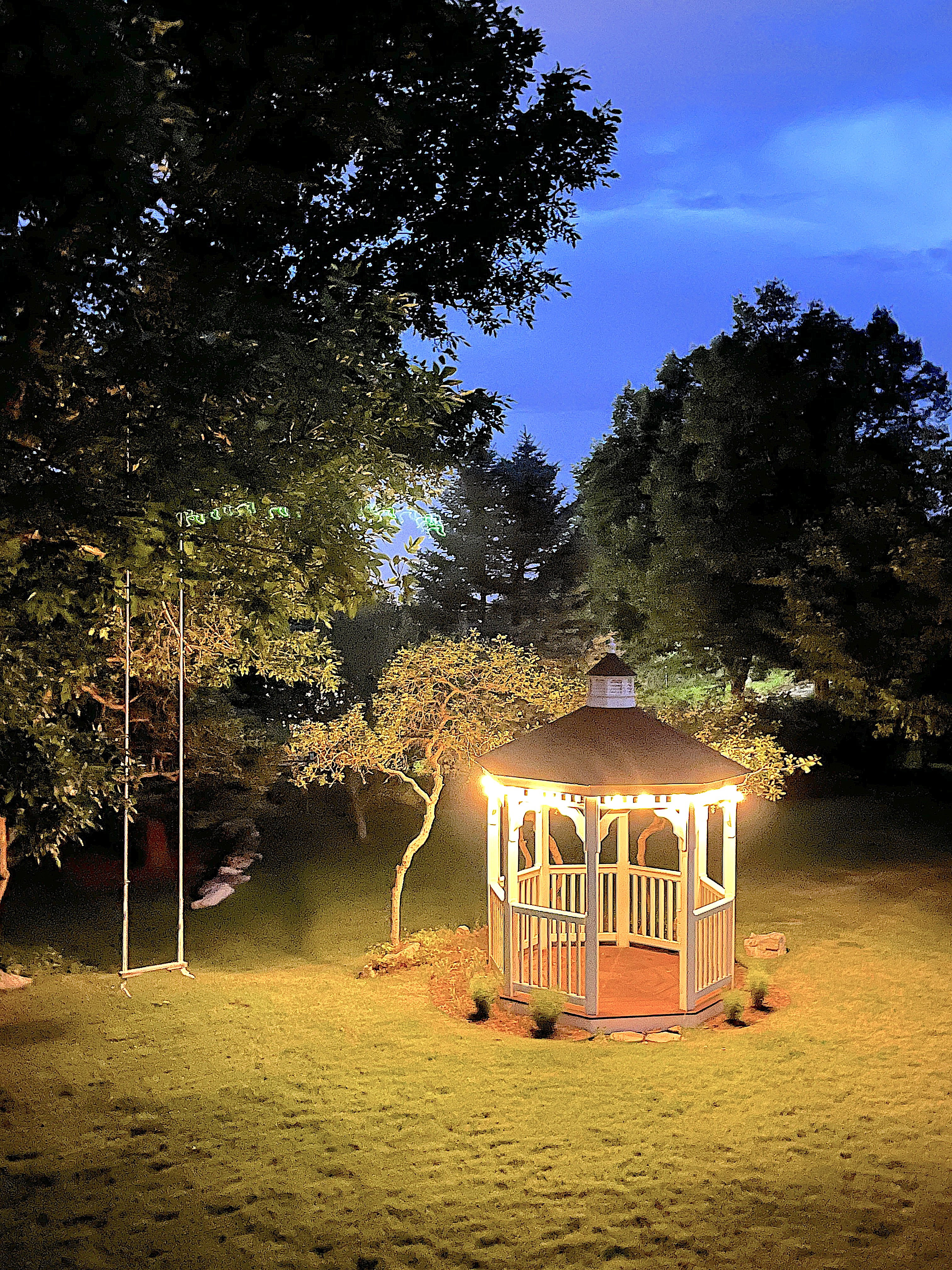 Illuminated backyard gazebo featuring a baluster railing, built-in string lighting, and a composite deck floor