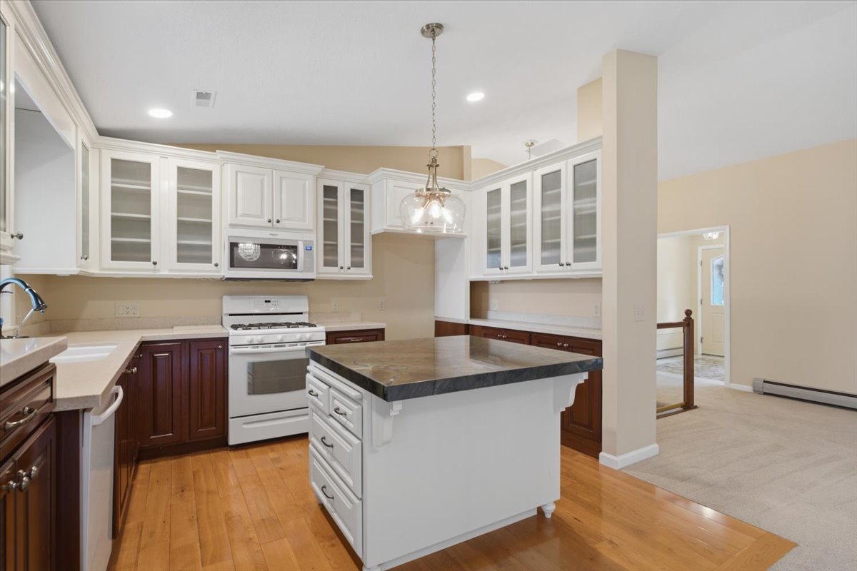 Kitchen featuring wood-finish flooring, two-tone cabinetry with glass-front upper cabinets, a center island with a dark countertop, a white gas range, and an integrated microwave