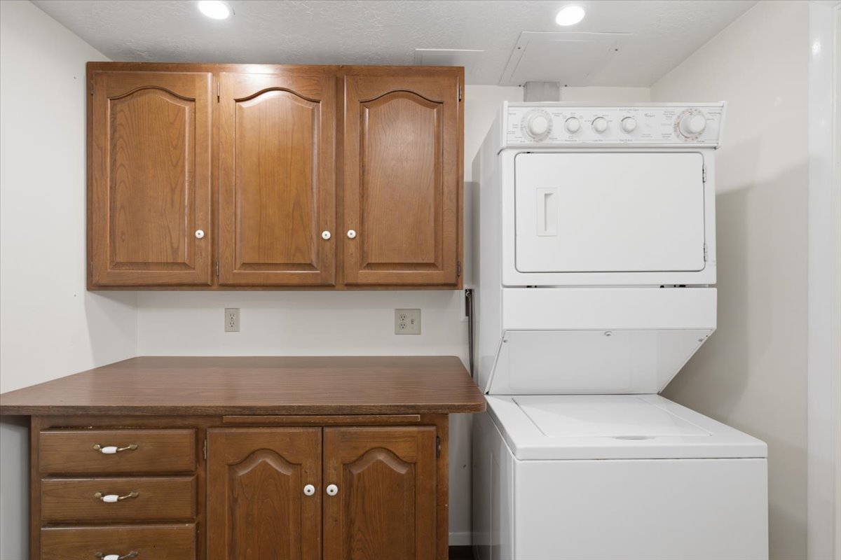 Dedicated laundry area featuring a stacked washer and dryer, wood-finish cabinetry, built-in countertop, and recessed lighting