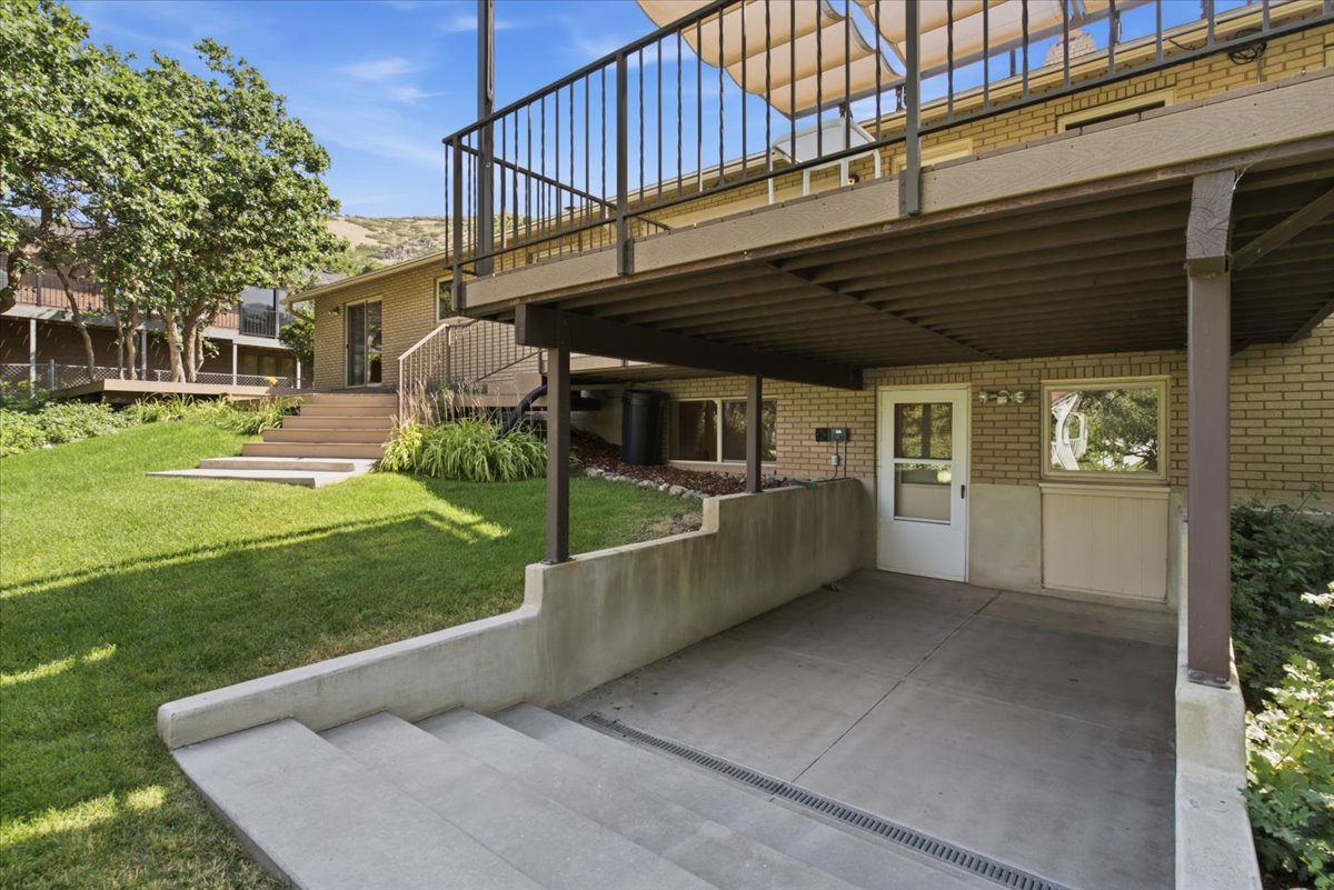 Concrete patio under an upper deck, featuring a white exterior door and brick facade