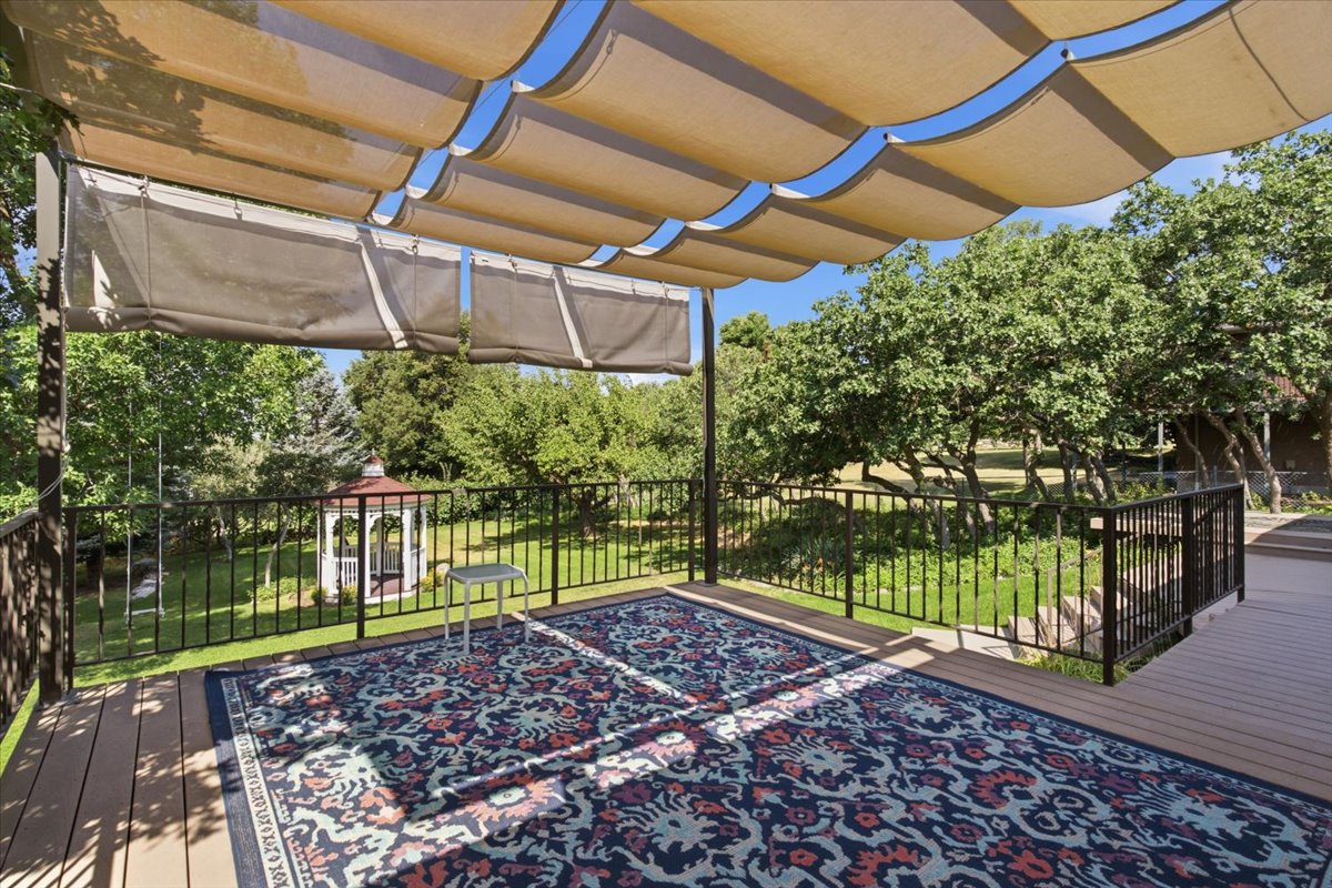 Expansive outdoor deck featuring wood-finish flooring, a retractable fabric canopy, and dark metal railings