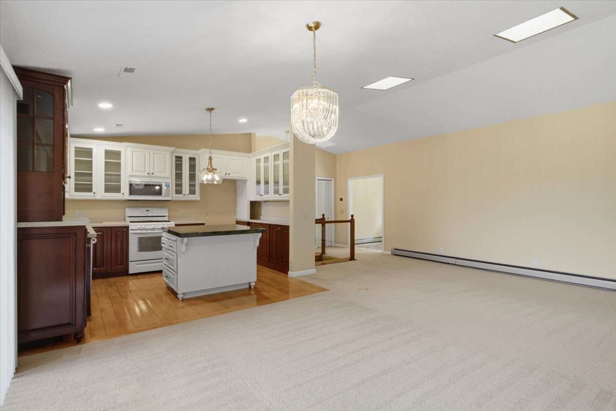 Open-concept living area featuring a kitchen with white and dark wood-finish cabinetry, a central island with a dark countertop, and a white range