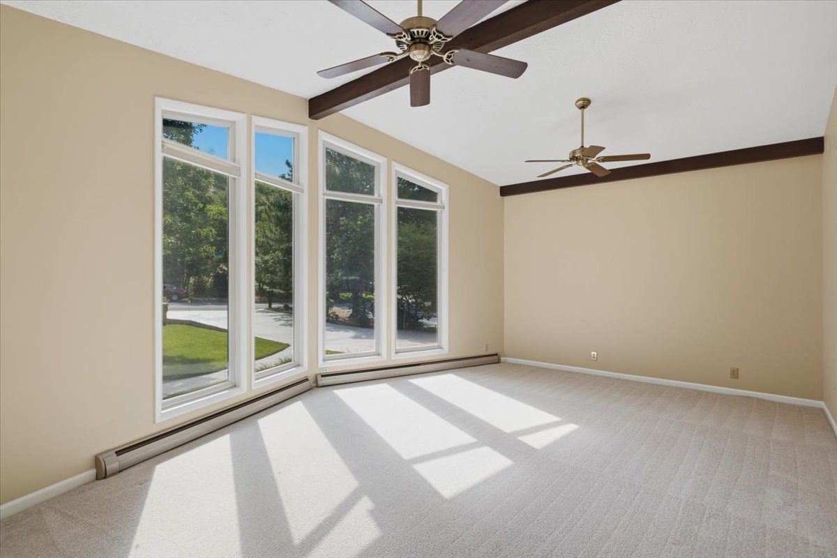 Expansive room featuring a wall of tall windows, light-toned carpeting, and a vaulted ceiling with exposed wood beams