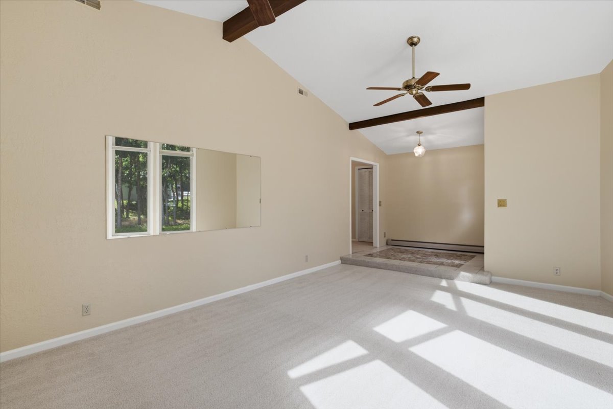 Vaulted ceiling with exposed wood beams, ceiling fan, and carpeted flooring