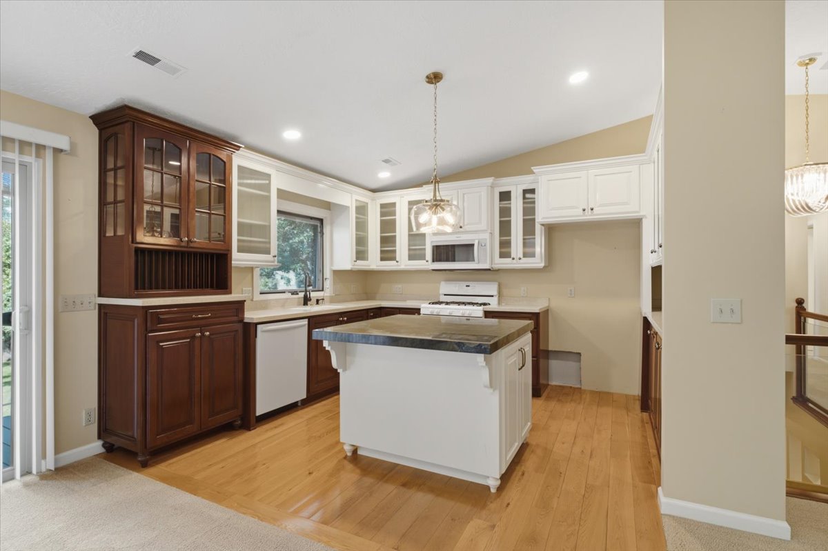 Open-concept kitchen featuring wood-finish flooring, a central island with a contrasting countertop, white upper cabinetry, and dark wood lower cabinetry
