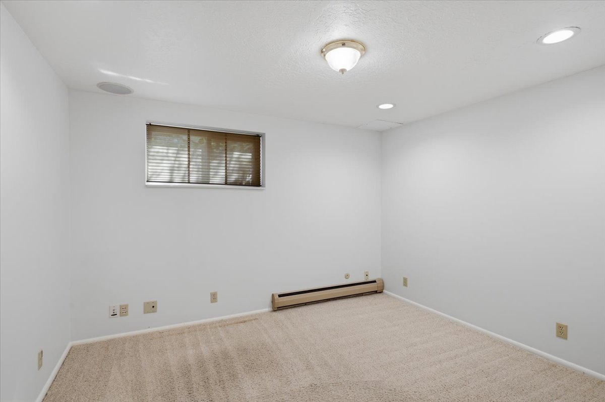 Carpeted room featuring a window with blinds, baseboard heating, a ceiling-mounted light fixture, recessed lighting, and a built-in ceiling speaker
