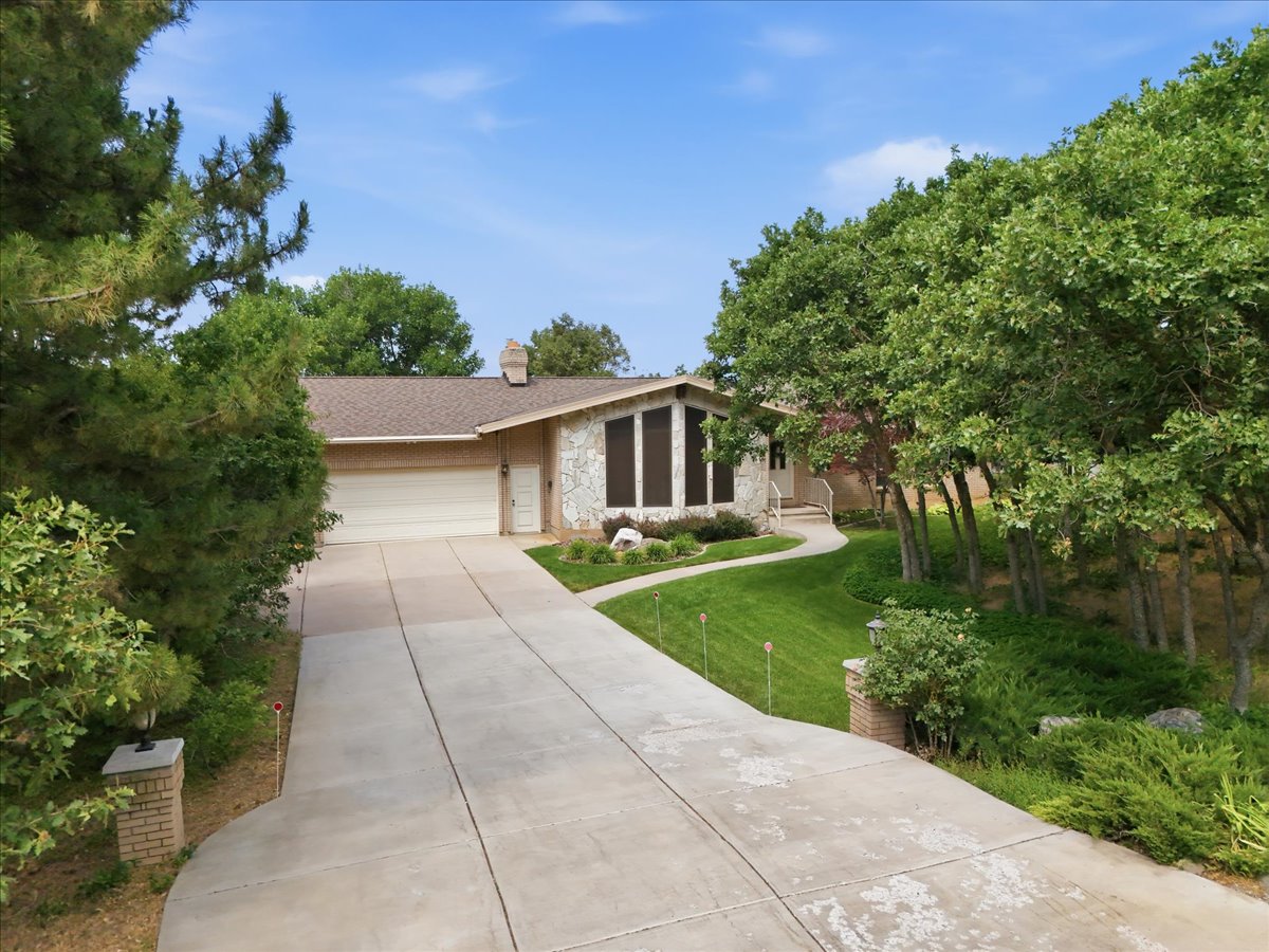 Ranch-style residence featuring a stone and siding exterior, an attached garage, a paved driveway, and mature landscaping