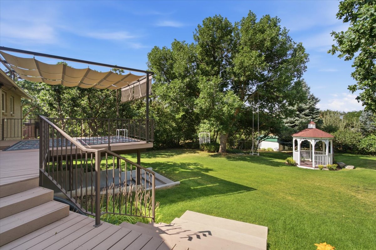 Expansive backyard featuring a manicured lawn, mature trees, and a white gazebo with a red roof