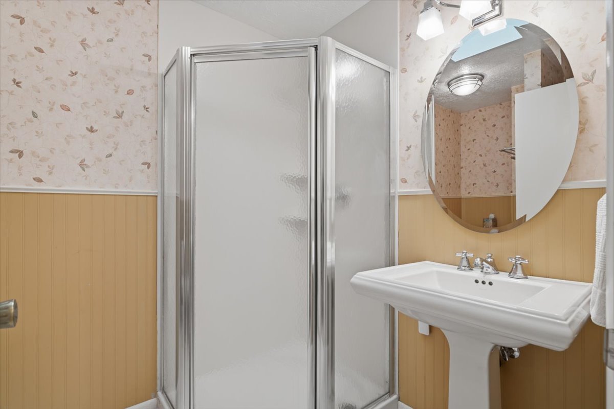 Pedestal sink with chrome faucet hardware, oval wall mirror, and overhead vanity lighting