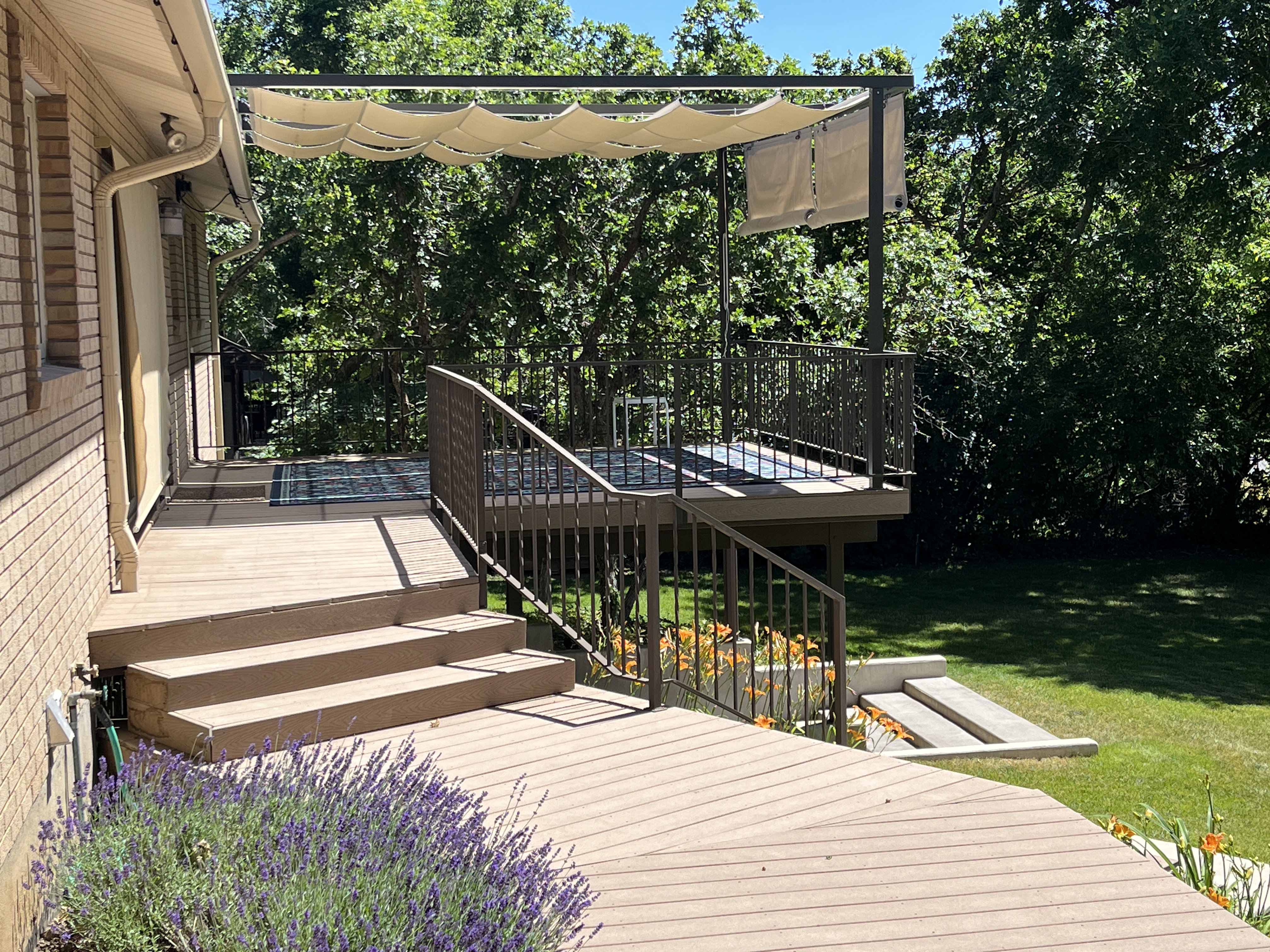 Multi-level deck featuring composite decking, dark metal railings, and a pergola with a retractable fabric canopy