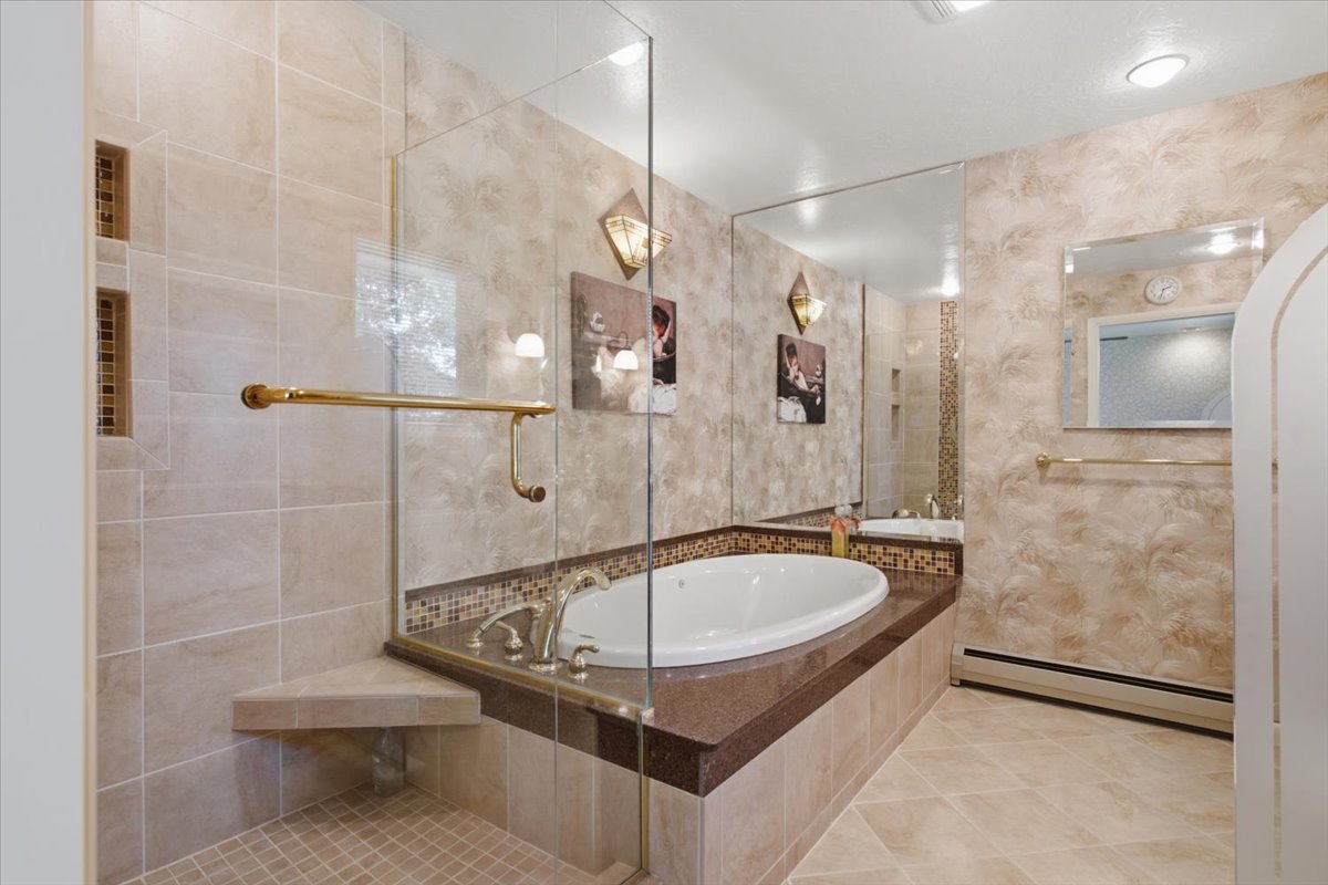 Tiled bathroom featuring a built-in jetted tub, glass-enclosed shower with a corner bench, and mosaic tile accents