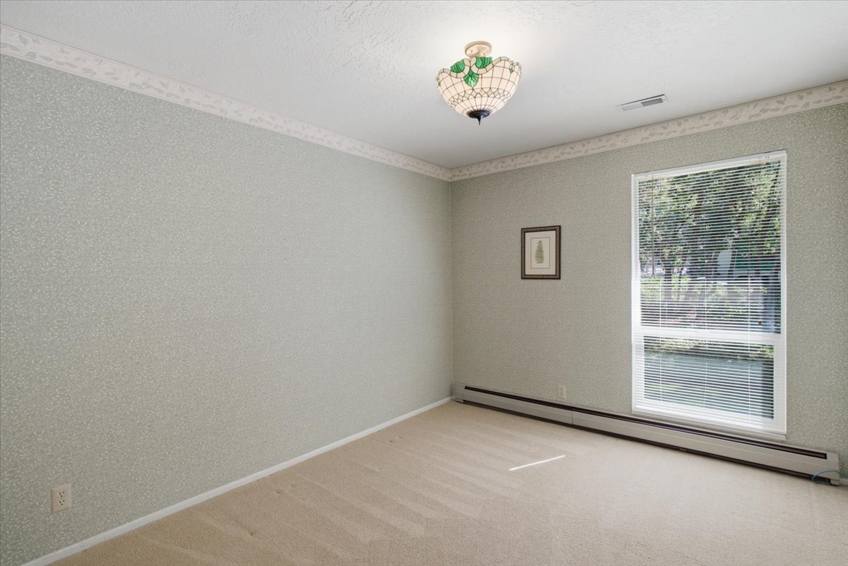 Carpeted room featuring a large window with blinds, baseboard heating, and a decorative ceiling fixture
