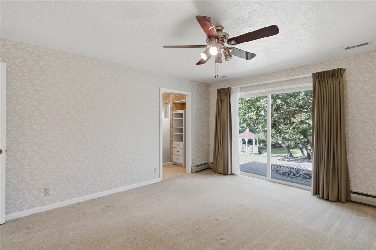 Room featuring a sliding glass door, patterned wallpaper, ceiling fan, and carpeted flooring