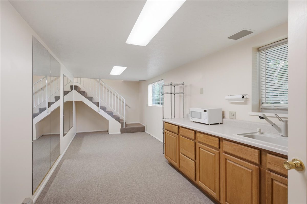 Lower level recreation space featuring a built-in wet bar with a single basin sink and wood-finish cabinetry