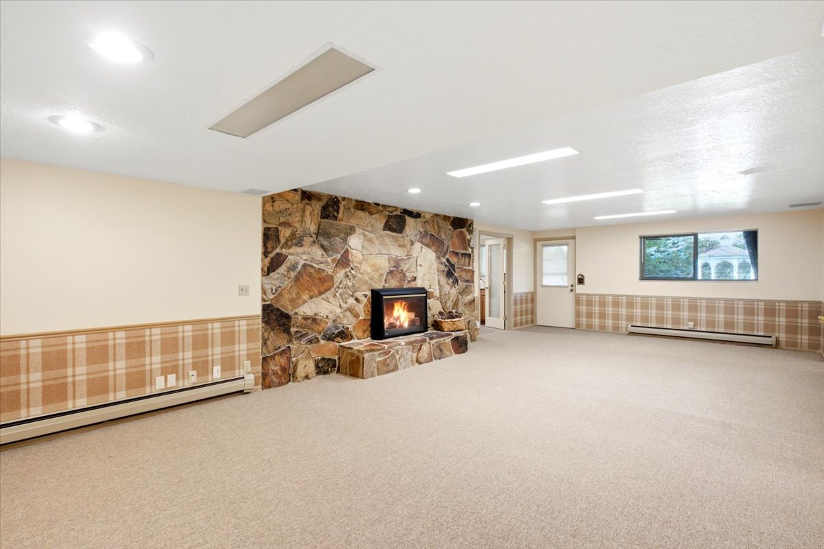 Spacious room featuring a stone fireplace with hearth, plush carpet flooring, recessed lighting, and a plaid wall accent