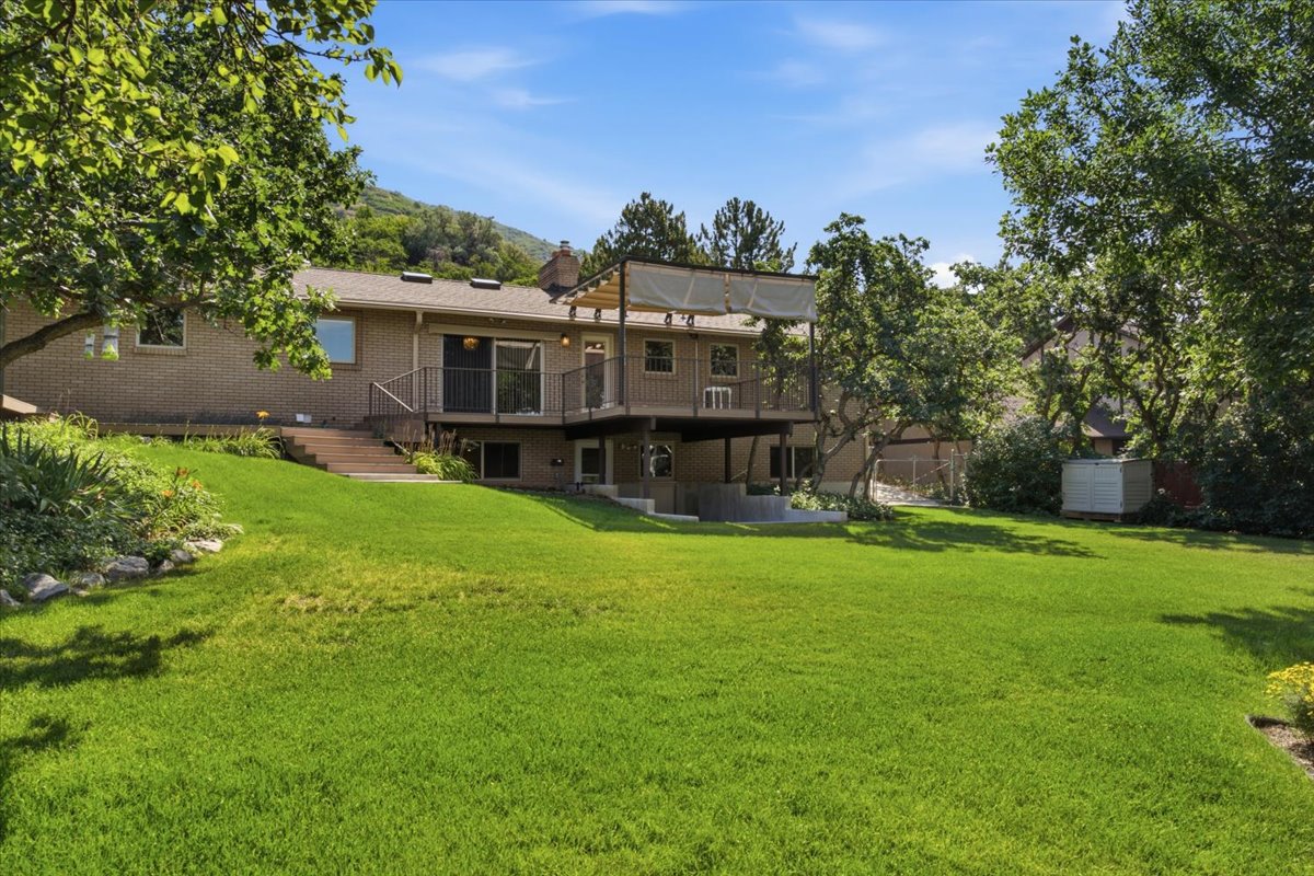 Spacious rear lawn featuring a tiered deck, lower patio area, and mature trees