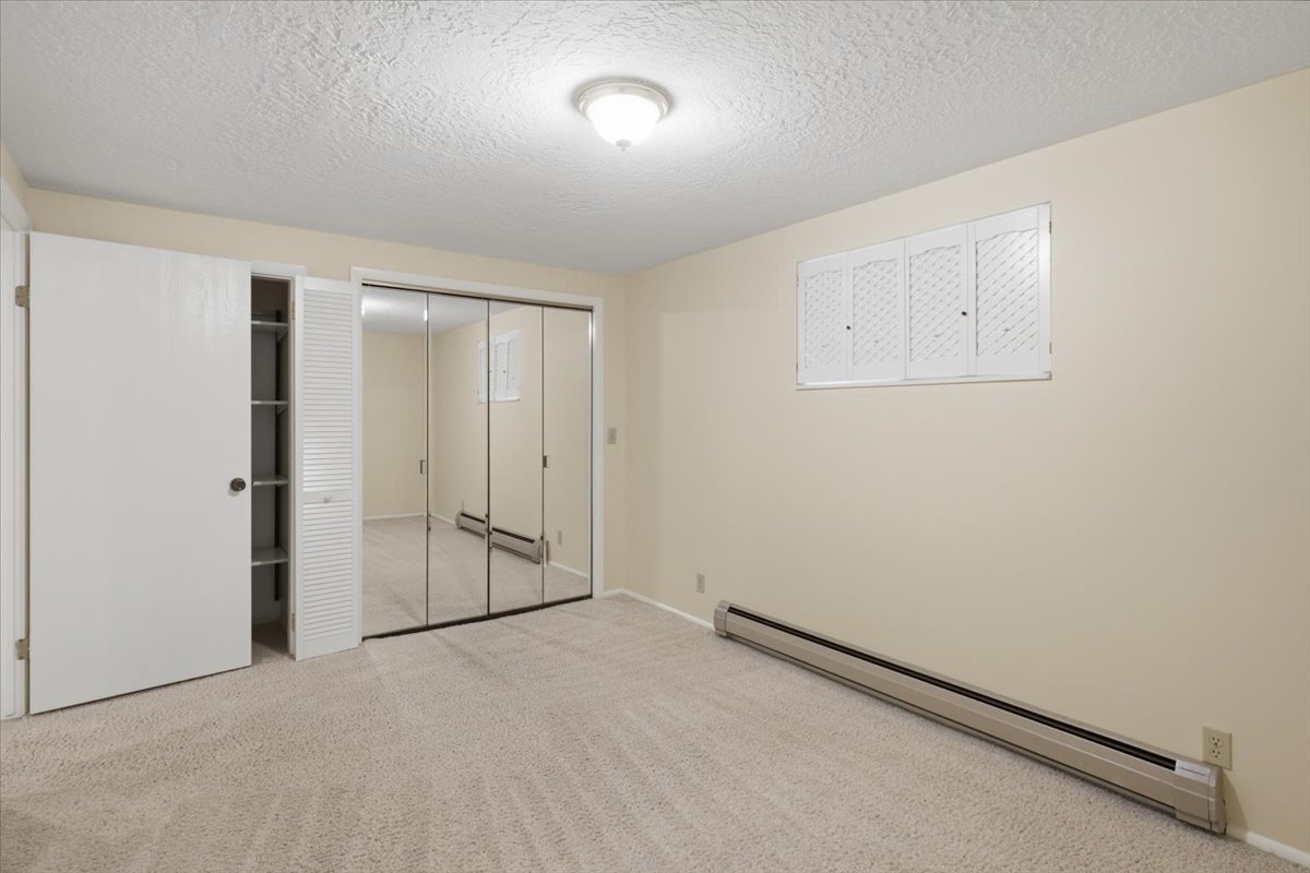 Carpeted room featuring a ceiling-mounted light fixture, baseboard heating, and an integrated closet with mirrored sliding doors